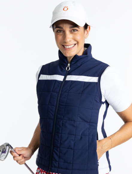 Smiling woman wearing the Chill Layer Golf Vest in Navy Blue, the Tee it Up Short Sleeve Golf Top in White, and the We've Got You Covered Hat in White. There is a solid, horizontal white stripe that runs across the front and back of this vest just above t
