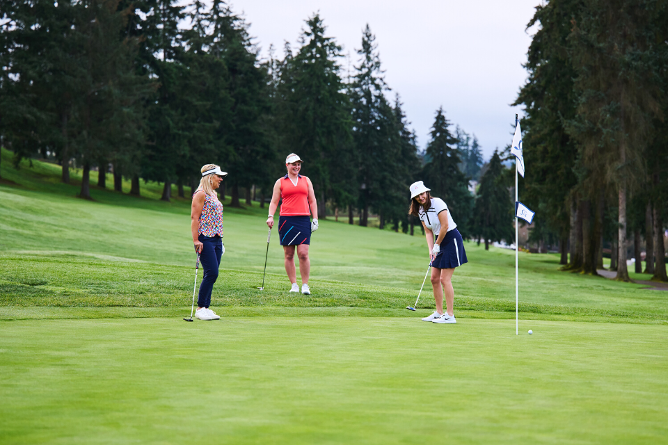 Three female golfers in KINONA sportswear finishing a put on the green grass course.