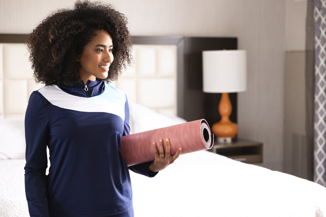 Woman wearing a navy blue long sleeve top with white contrast and holding a pink yoga mat