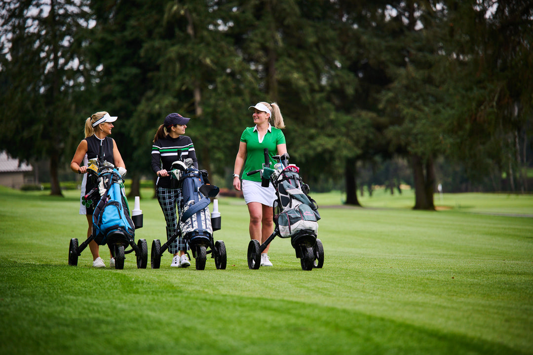 Three women on the golf course push golf bags on carts