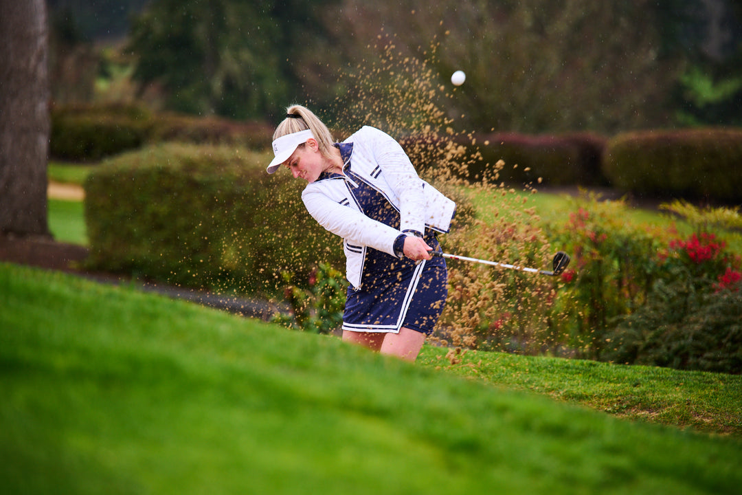 women in golf jacket hitting ball out of sand trap