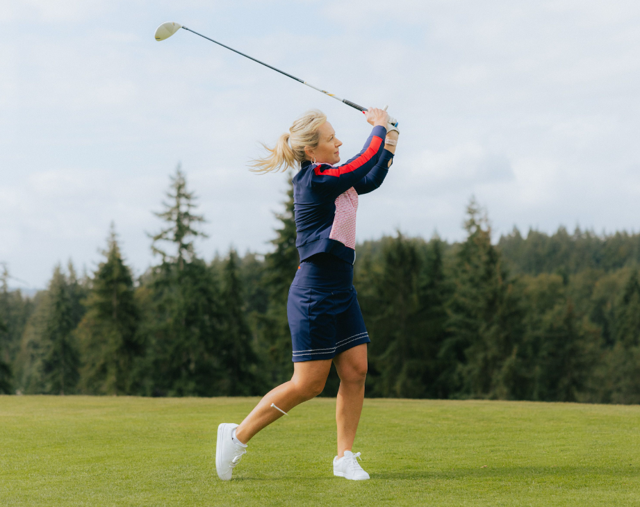 A woman wearing a dark blue skirt and long-sleeved shirt, swinging a golf club