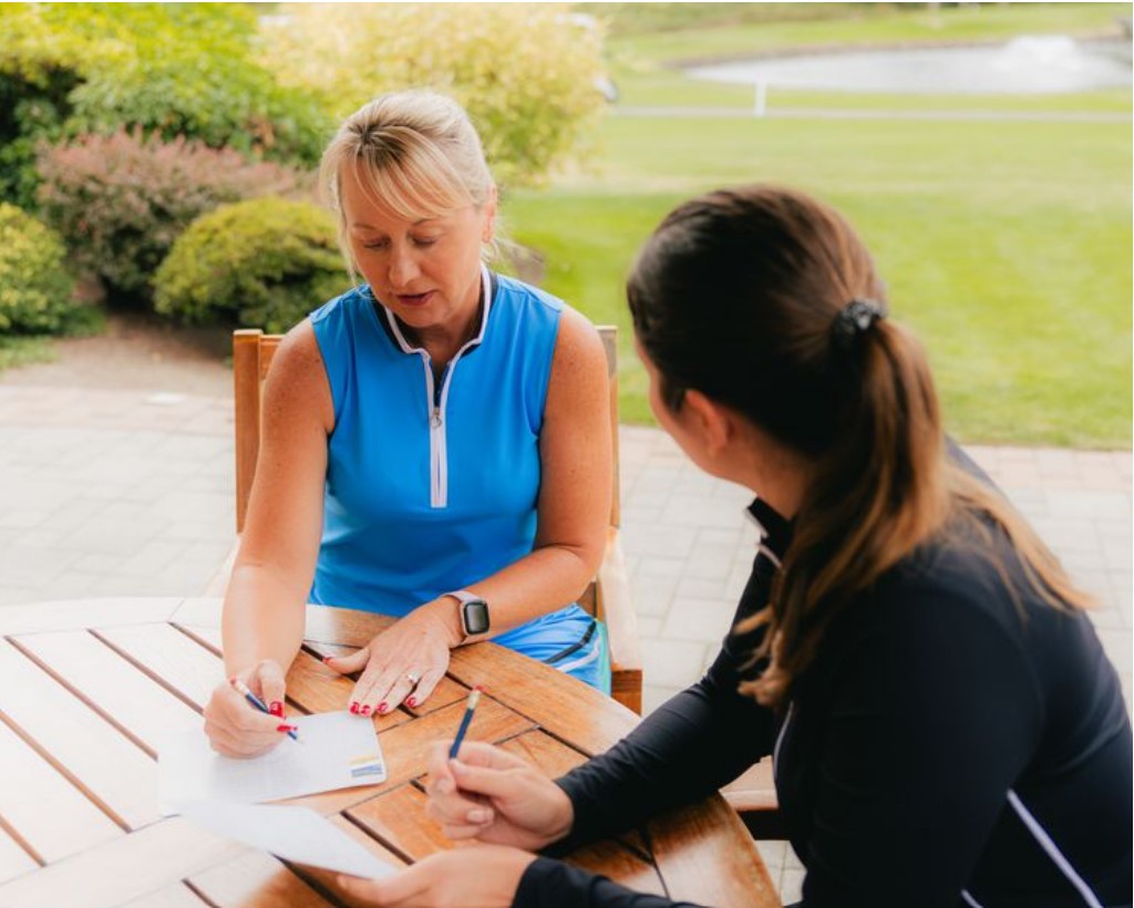 Two women sitting a wooden table, tallying scores 