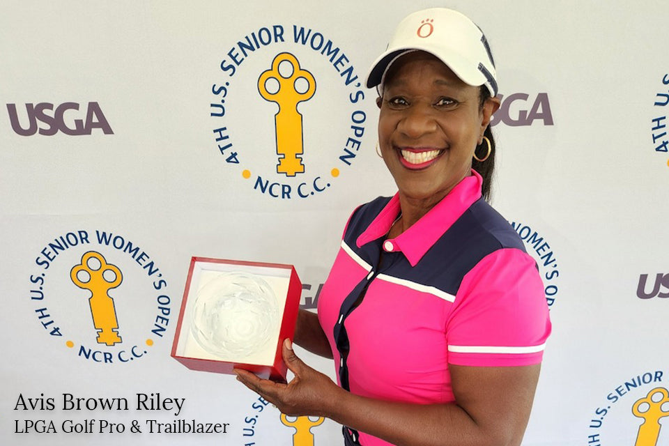 Avis Brown-Riley smiling with a LPGA award in a pink and blue KINONA top and hat.