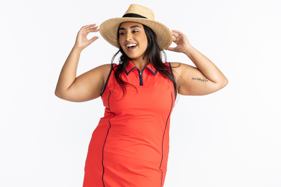 A smiling woman in a an orange dress and straw hat representing the plus-size female for KINONA.