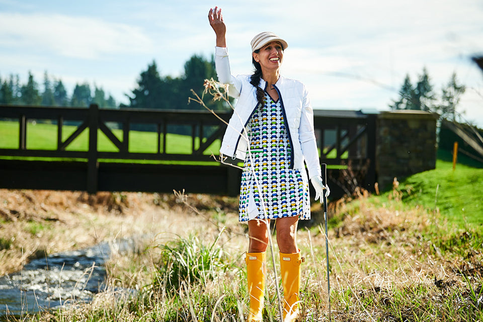 A female golfer holding up her found ball in the rough wearing a plaid KINONA dress.