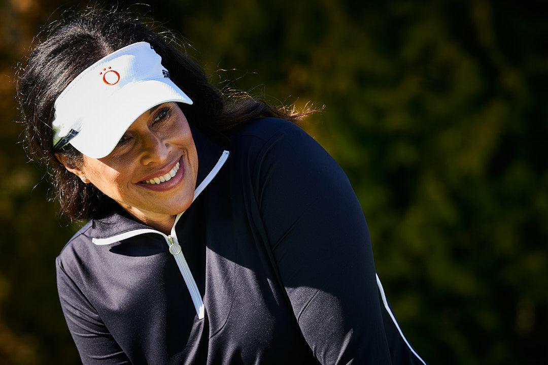 A female golfer smiling down the line of a sunk putt in KINONA visor and pullover.
