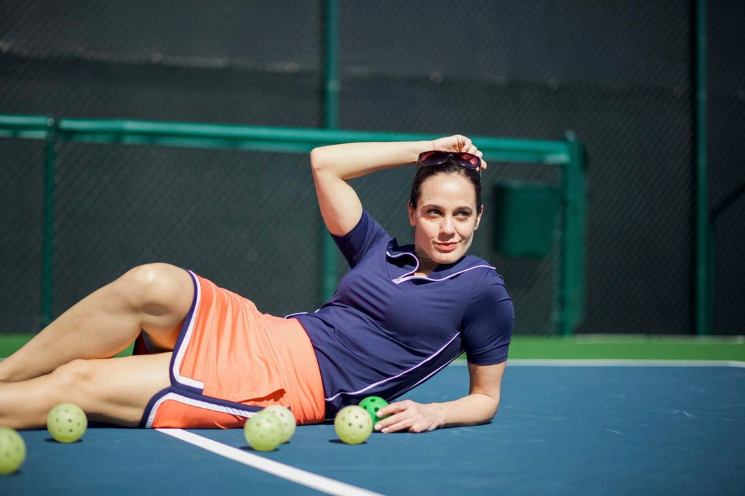 A woman lying down on pickleball court after match in Blue and Orange KINONA apparel.