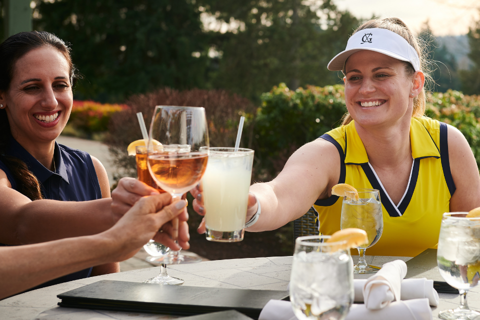Three female golfers smiling at the 19th hole with a cheers of drinks in yellow and blue KINONA attire.