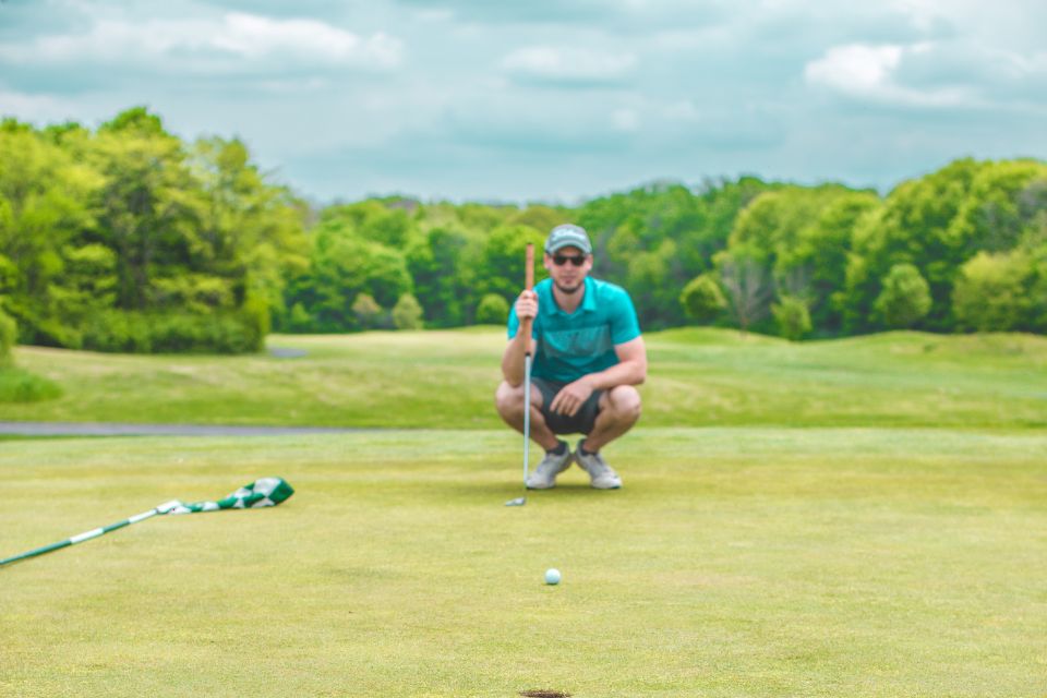 A male golfer kneeling down to measure his shot on the green.