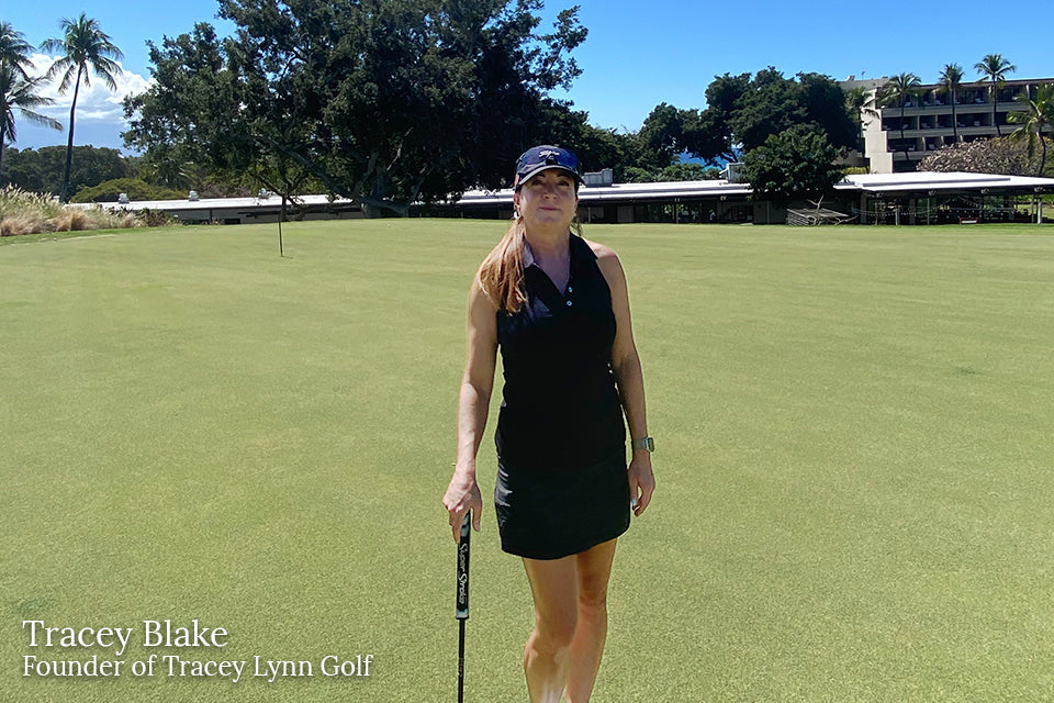 Tracy Blake smiling on green grass course in a black KINONA golf dress.