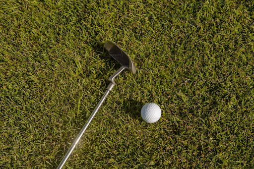 A golf club and golf ball laying on thick green grass