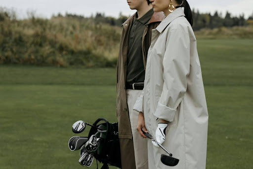 A man and woman standing on a golf course wearing coats