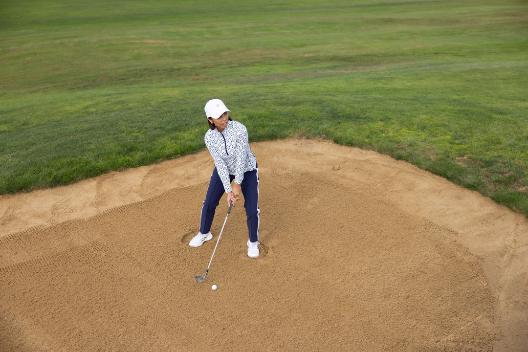 A woman on a golf course about to hit a ball. 