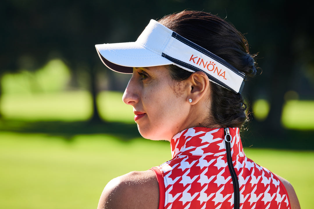 A female golfer looking down the fairway to her left in white KINONA visor.