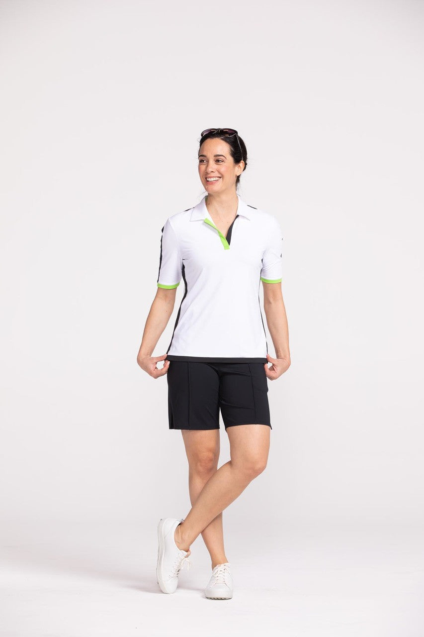 Full view of a woman golfer wearing a white Keep it Covered short sleeve golf top with black Tailored and Trim golf shorts