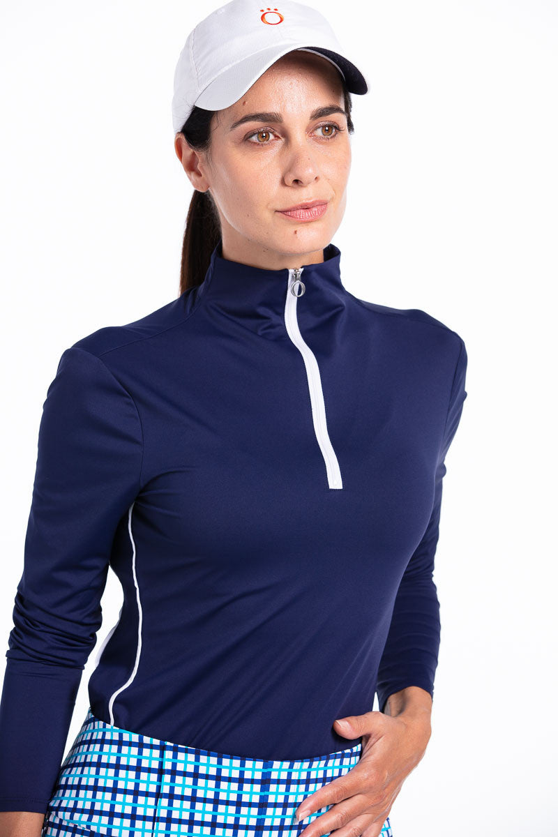 Woman golfer wearing a navy blue Keep It  Covered longsleeve golf top, blue check shorts, and a white We've Got You Covered golf hat.