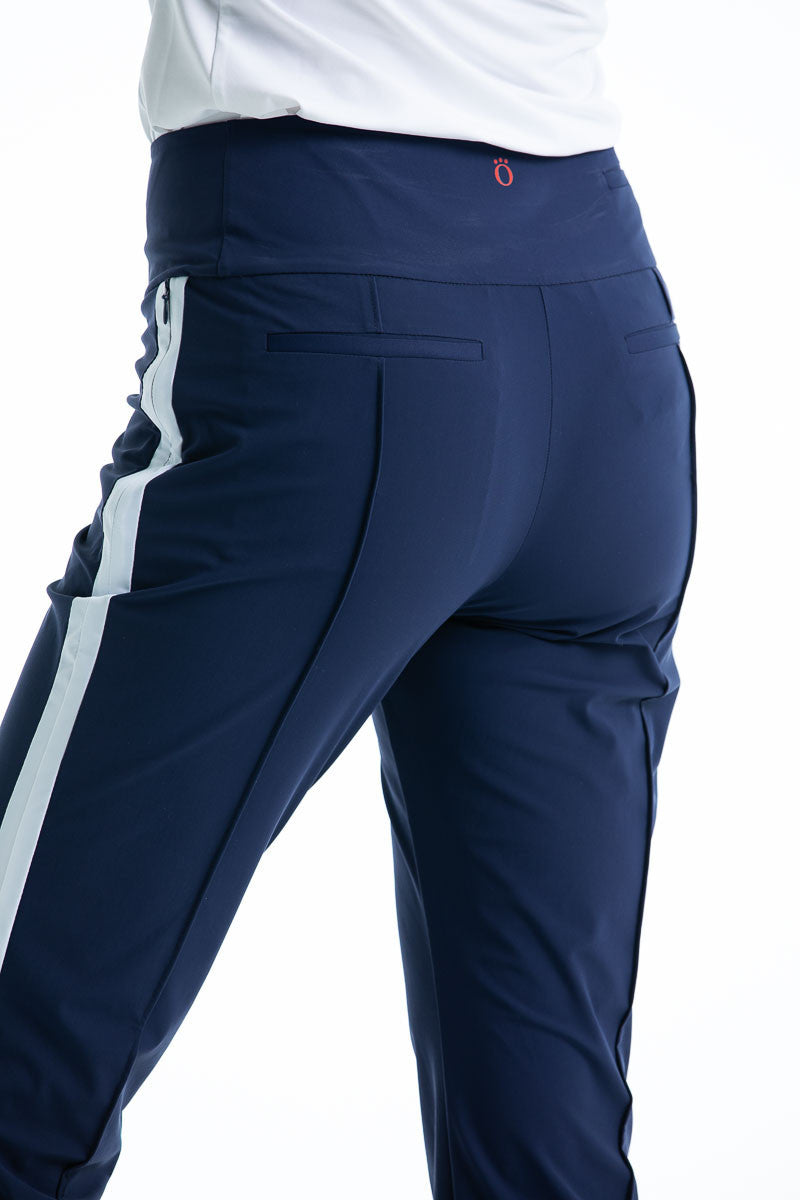 Back view of woman in navy blue Tailored Track golf pants with white trim down the side of the leg.