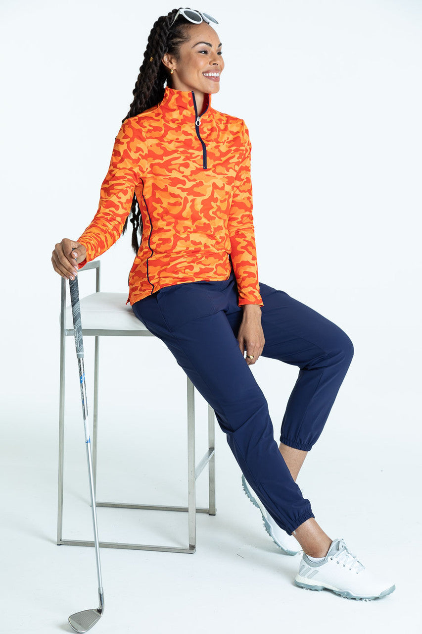 Female golfer wearing a hidden in site orange Keep It Covered Long Sleeve top and navy blue Tailored and Trim Jogger golf pants