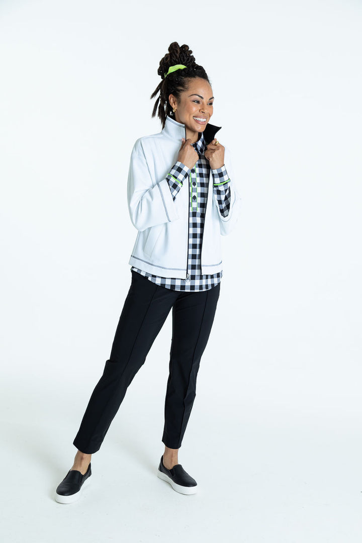Full view of a woman wearing a white To the Nines golf jacket, a buffalo check At the Pin long sleeve golf shirt, and black Smooth Your Waist crop golf pants