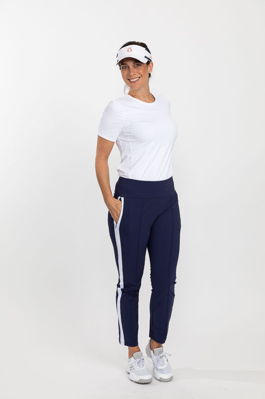 Full front and side view of a woman wearing a white No Hat Hair Visor, a Tee It Up Short Sleeve Golf Shirt in white, and a pair of Tailored Track Golf Pant in navy blue