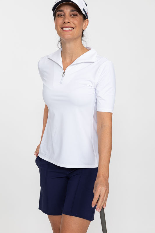 Front view of a smiling woman leaning on a golf club wearing a white No Hat Hair Visor, a Keep It Covered Short Sleeve Golf Top in white/white, and a Wrap It Up Golf Skort in navy blue