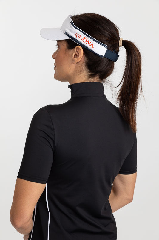 Back view of a woman wearing a white No Hat Hair Visor and a Keep It Covered Short Sleeve Golf Top in black