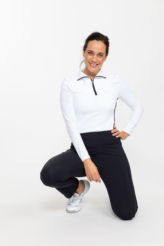 Smiling woman crouched down wearing a Keep It Covered Long Sleeve Golf Top in white and a pair of Smooth Your Waist Crop Golf Pants in black