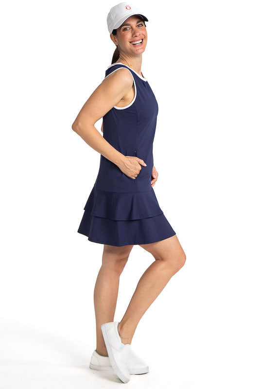 Full right view of a smiling woman wearing the On In Two Sleeveless Golf Dress in Navy Blue and a We've Got You Covered baseball cap in white.