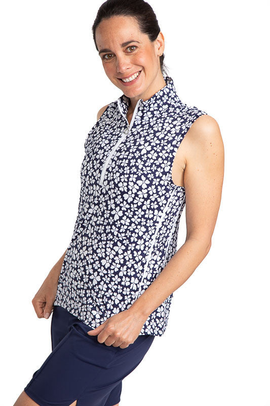 Full front view of a smiling woman wearing the Keep It Covered Sleeveless Golf Top in Vinca Print. The Vinca print has a navy blue background with white flowers on it.