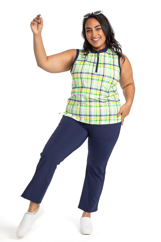 Full front view of a smiling woman raising her right hand in the air wearing the Zip It and Rip It Sleeveless Golf Top in Picnic Plaid and the Smooth Your Waist Crop Pants in navy blue. This plaid includes white, navy blue, yellow, and green in the print.