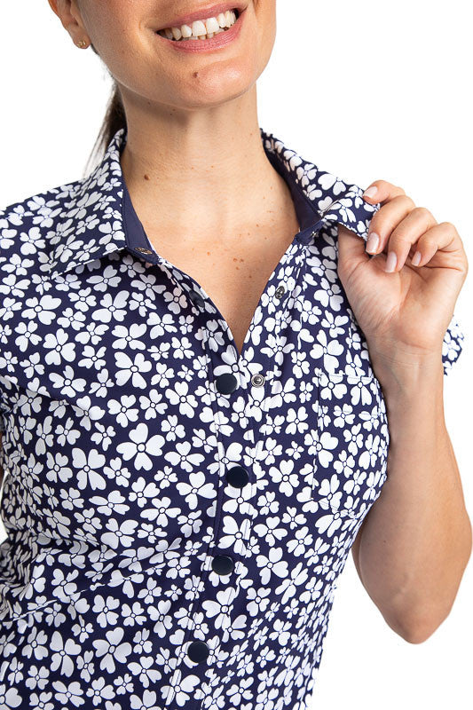 Close front view of the neckline of the Tough in the Rough Short Sleeve Golf Top in Vinca Print. The Vinca print consists of a navy blue background with small, white flowers on it.