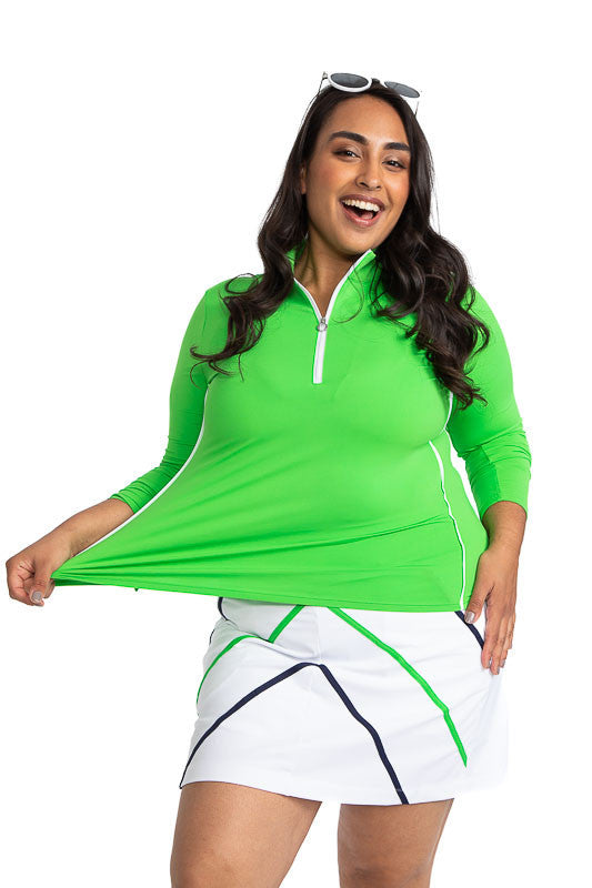 Full front view of a smiling woman wearing the Keep It Covered Long Sleeve Golf Top in Fairway Green, and the Show Me The Way Golf Skort in White. This skort also has accents of Navy Blue and Fairway Green on it.