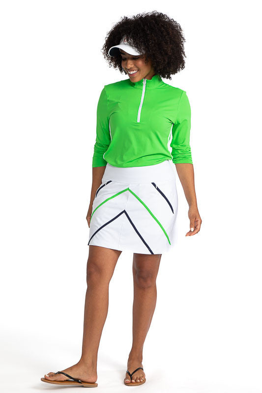 Full front view of a woman wearing the Keep It Covered Long Sleeve Golf Top in Fairway Green, the No Hat Hair Visor in White, and the Show Me The Way Golf Skort in White. This skort has accents of Fairway Green and Navy Blue on it.