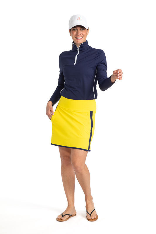 Smiling woman wearing the My Go To Golf Skort in Lemon Yellow, the Keep It Covered Long Sleeve Golf Top in Navy Blue, and The Big O Hat (baseball-style hat) in White. This skort has navy blue accents on each side and along the hemline.