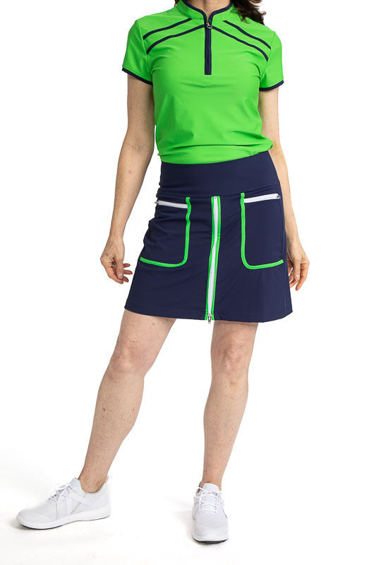 Complete front view of a woman wearing the Ready Play Golf Skort in Navy Blue, and the Gimme Putt Short Sleeve Golf Top in Fairway Green. This golf skort also has Fairway Green accents down the length of the zipper on both sides, a white front zipper, Fai