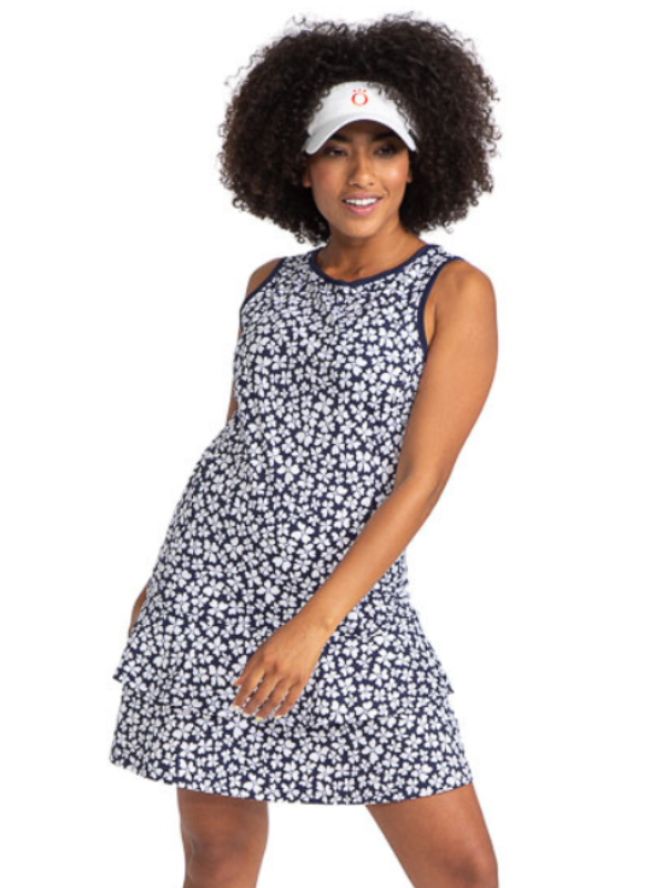 Front view of woman golfer wearing the On In Two sleeveless golf dress in Vinca Print and a white No Hat Hair Visor in white. Women's floral golf dress.