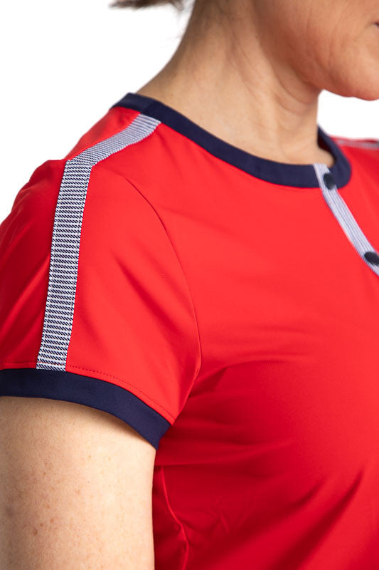 Close side right view of the shoulder of the Approach Shot Short Sleeve Golf Top in Cherry Red. This top has navy blue accents around each arm, the neckline, and the buttons on the front. The front is also accented with Workin' It Stripe across the top of