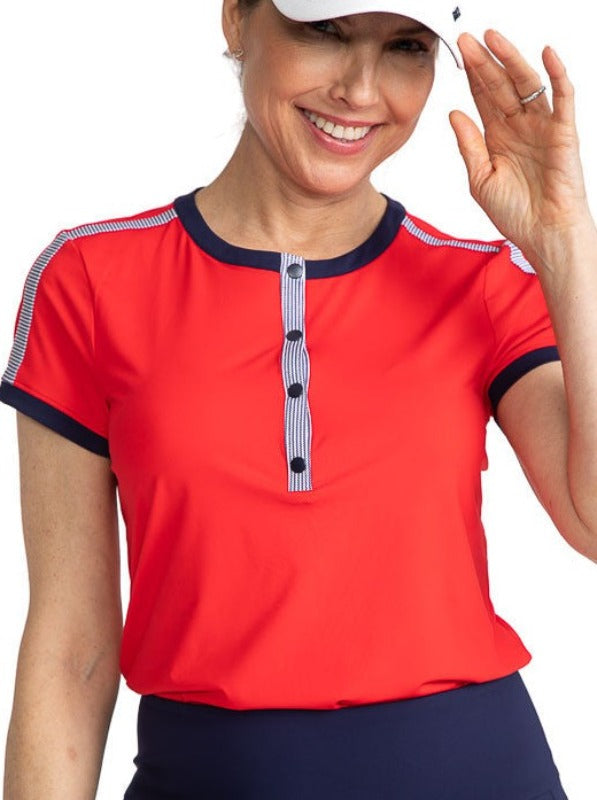 Smiling woman wearing the Approach Shot Short Sleeve Golf Top in Cherry Red. This top has navy blue accents around each arm, the neckline, and the buttons on the front. The front is also accented with Workin' It Stripe across the top of each shoulder and 
