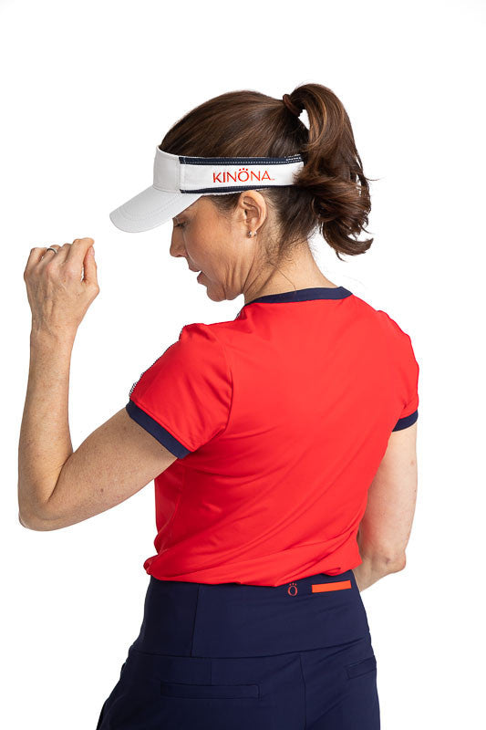 Full back and left side view of the Approach Shot Short Sleeve Golf Top in Cherry Red. This top has navy blue accents around each arm, the neckline, and the buttons on the front. The front is also accented with Workin' It Stripe across the top of each sho