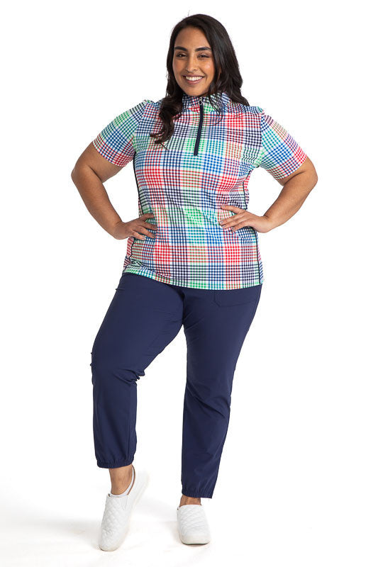 Complete front view of a smiling woman with her hands on her hips wearing the Keep It Covered Short Sleeve Golf Top in Vacation Plaid and the Smooth Your Waist Crop Pants in Navy Blue. Vacation Plaid consists of a small, checkered pattern of red, blue, gr