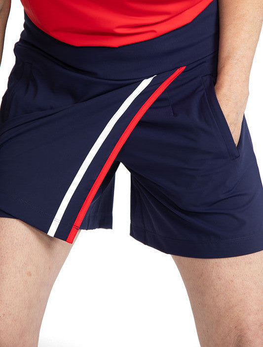 Close front view of the Skort and Short Golf Skort in Navy Blue. Here you can see the shorts under the skirt portion of the skort along with the two stripes - one in white and one in cherry red - on the left side of the skort. You can also see the left si