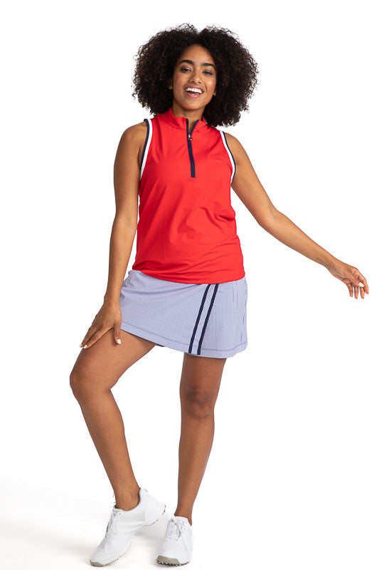 Complete front view of a smiling woman wearing the Skort and Short Golf Skort in Workin' It Stripe and the Love the Sun Sleeveless Golf Top in Cherry Red. This stripe pattern consists of navy blue stripes on a white background. This skort has two vertical