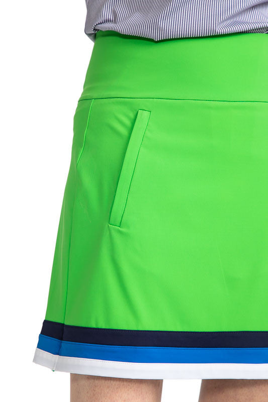 Close front and right side view of the On the Fringe Golf Skort in Fairway Green. This skort has three stripes around the bottom of this skort in Navy Blue, Azure Blue, and White. 