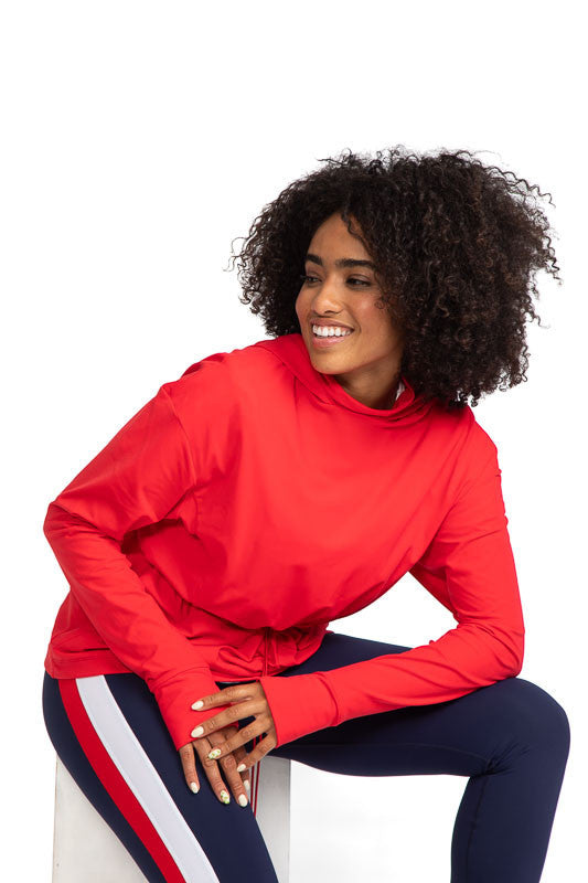 Smiling woman wearing the Apres 18 Anorak Long Sleeve Hoodie in Watermelon Red and the Apres 18 Striped Leggings in Navy Blue.