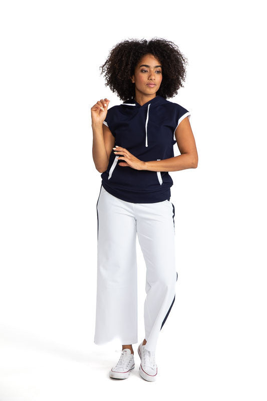 Smiling woman wearing the Apres 18 Extended Shoulder Hoodie in Navy Blue and the Apres 18 Wide Leg Pants in White.