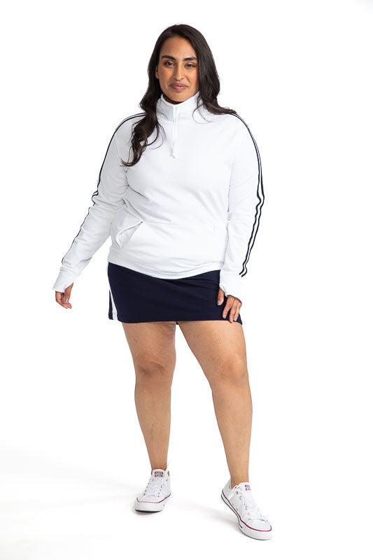 Complete front view of a woman wearing the Apres 18 Funnel Neck Long Sleeve Top in White and the Apres 18 Sport Skirt in Navy Blue. This top has two navy blue stripes down each arm. 