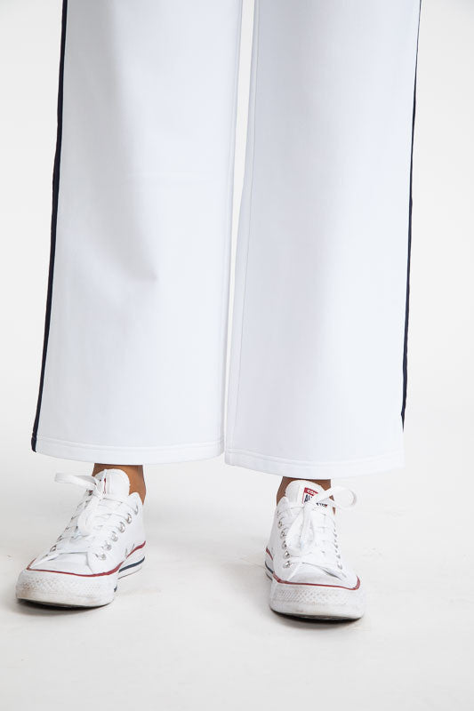 Close front view of the hemline on the  Apres 18 Wide Leg Pants in White. These pants have a navy blue stripe down each side. 