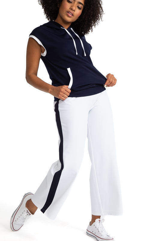 Smiling woman wearing the  Apres 18 Wide Leg Pants in White and the Apres 18 Extended Shoulder Hoodie in Navy Blue. These pants have a navy blue stripe down each side. 