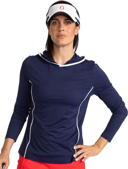 Front view of a woman golfer wearing the Layer It Up Long Sleeve Hoodie Golf Top in Navy Blue and the No Hat Hair Visor in White. There are white accents around the edge of the hood and down each side of this hoodie.